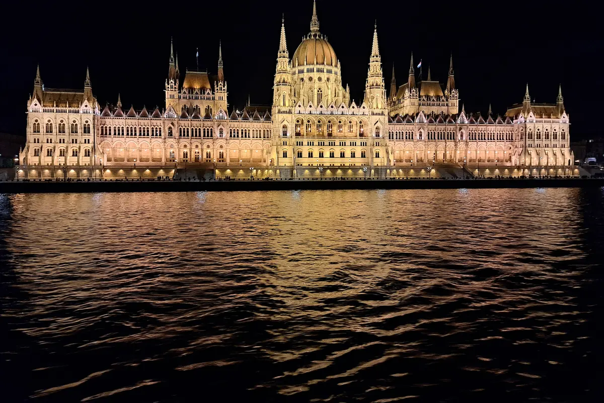 The long facade of the Hungarian Parliament Building lit at night and reflected in the dark Danube.