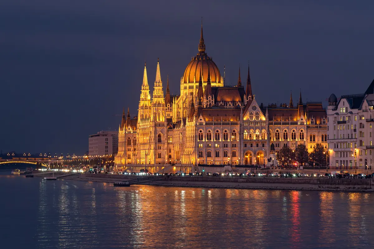 The Hungarian Parliament Building at twilight, its dome lit gold above the Danube, with Margit Bridge faintly visible on the left.